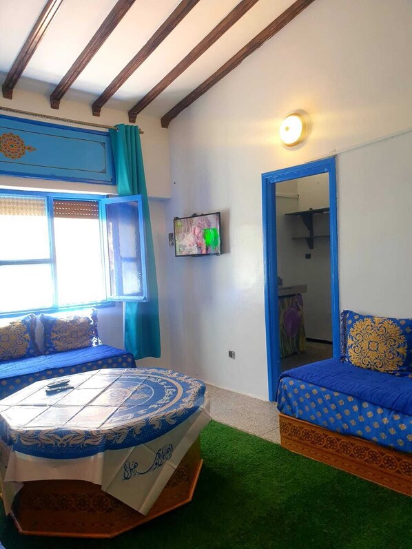 Una habitación con una cama de diseño azul y blanco, una mesita con un cubre decorativo, un televisor montado en la pared y un espejo.