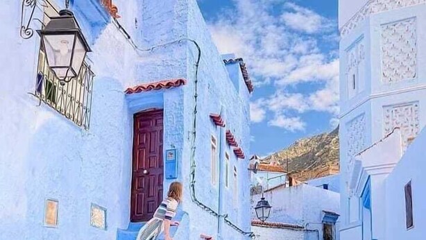 Una calle estrecha con edificios blancos, una puerta roja y una persona bajando escaleras.