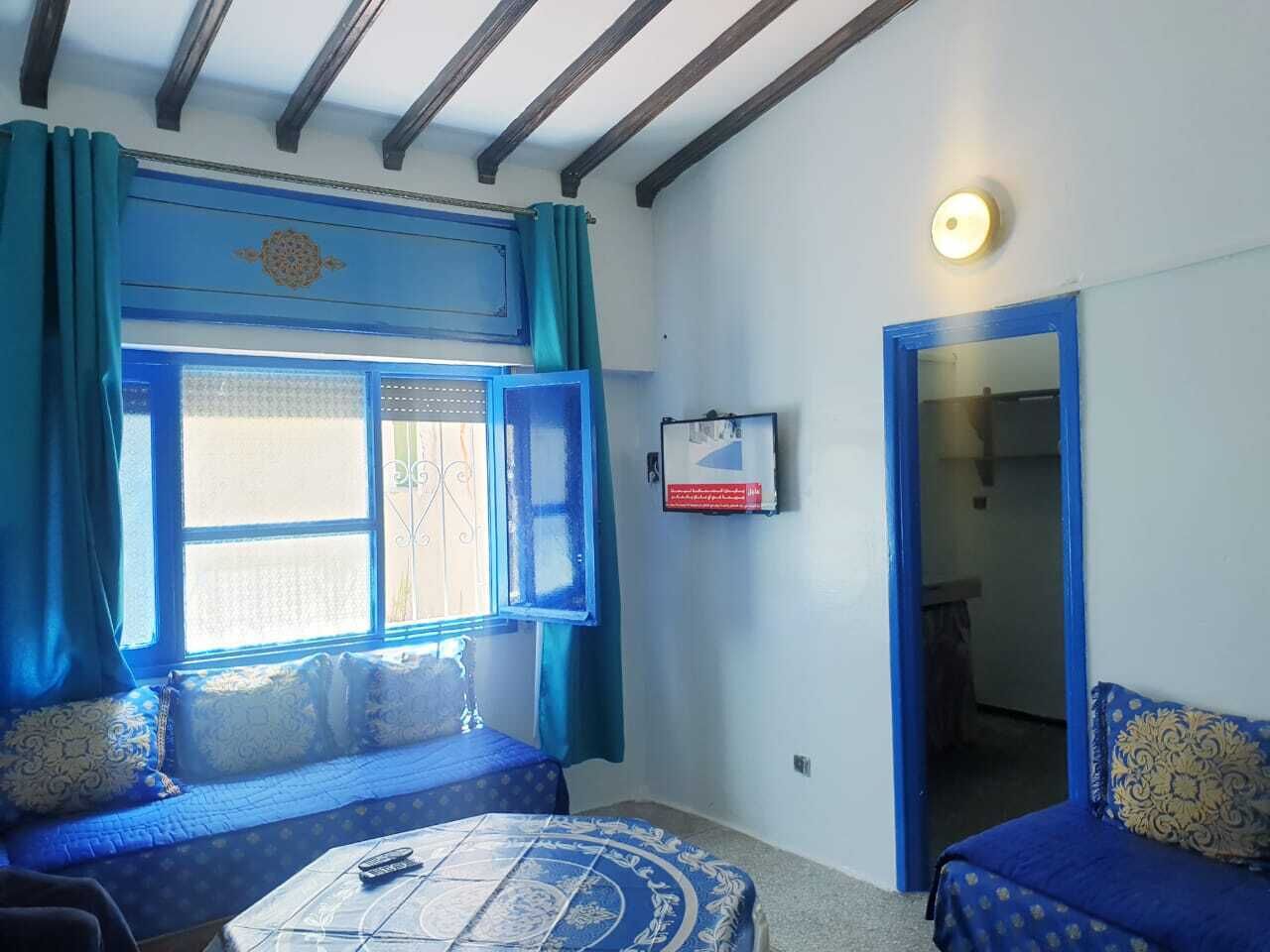 Una habitación con dos camas, una mesa y un ventanal con cortinas.