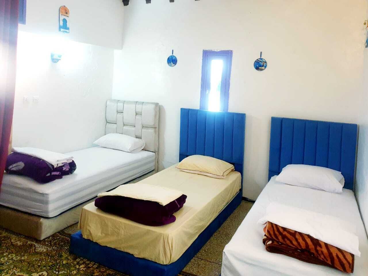 Una camera d'albergo con tre letti singoli, ognuno con una testiera di colore diverso.