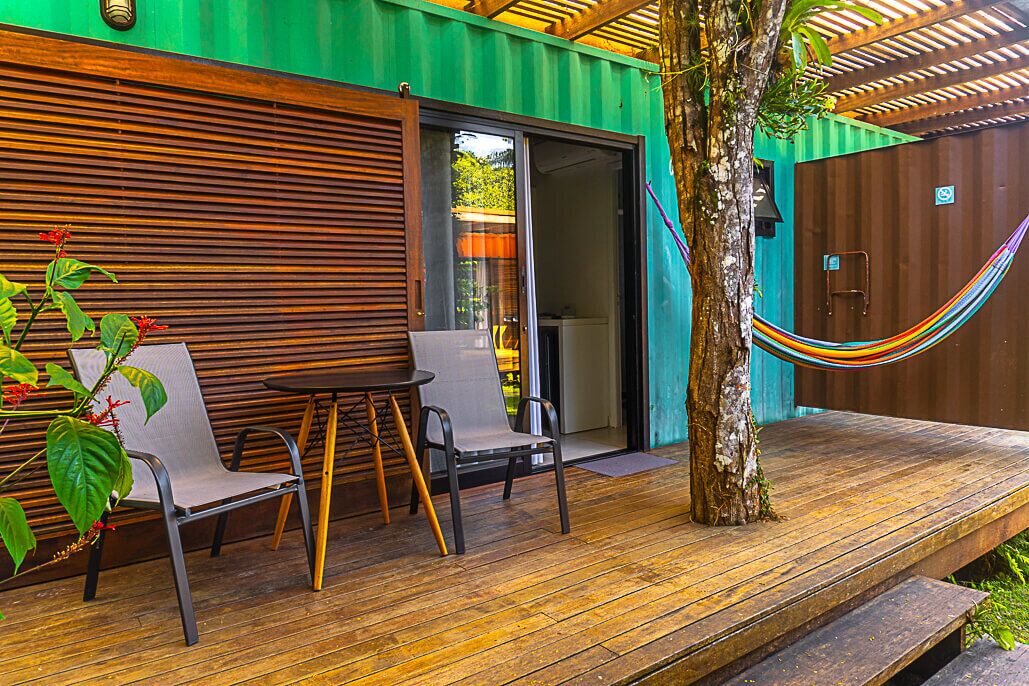 An outdoor patio with a wooden deck, two chairs, a small table, and a hammock.