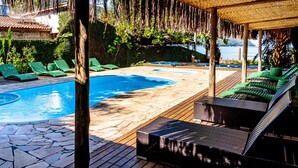 Ein Poolbereich mit Holzterrasse, Liegestühlen und einer strohgedeckten Struktur.