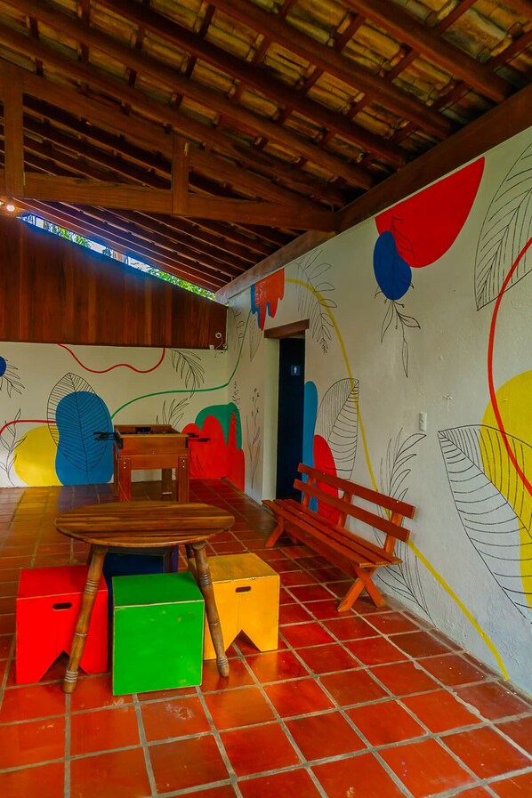 A room with a wooden table, colorful stools, and a wall with abstract leaf patterns. - Pousada Vila Jacaa (Ubatuba)