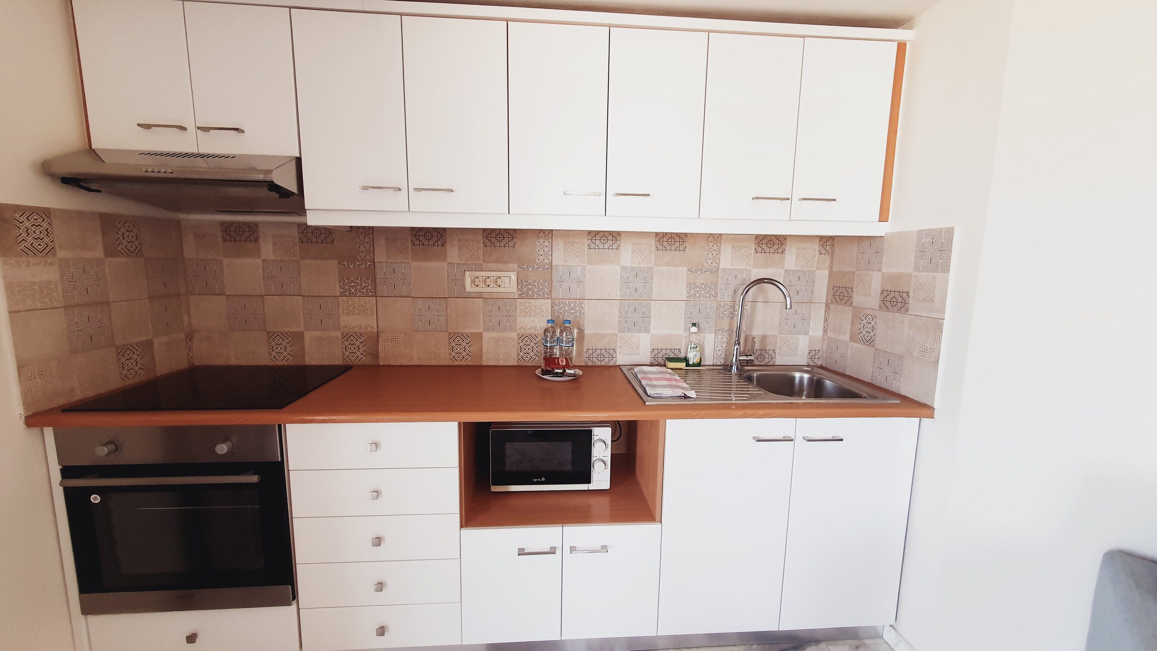 Een kleine keuken met witte kastjes, een magnetron, een fornuis en een spoelbak.