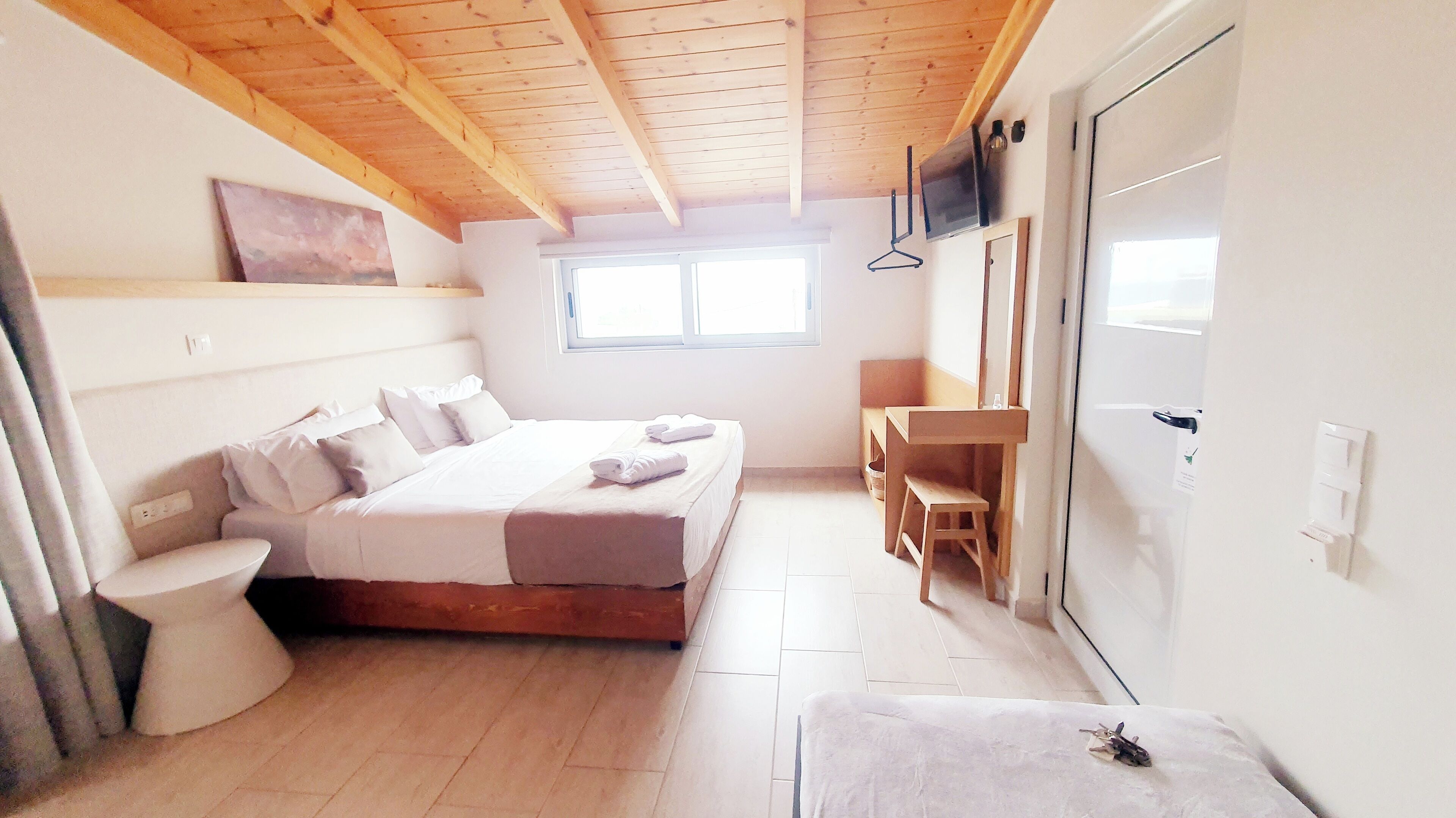 A bedroom with a wooden ceiling, a bed, a bedside table, a chair, a toilet, and a window.