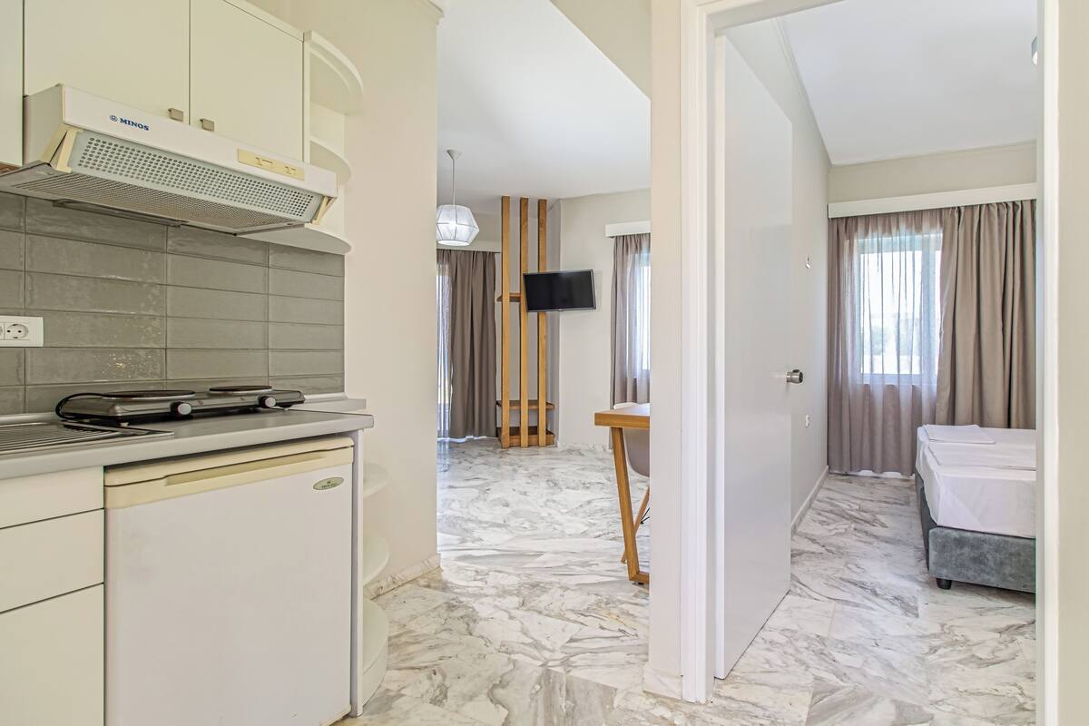 A modern hotel room with a kitchen area, a dining table, and a bed.
