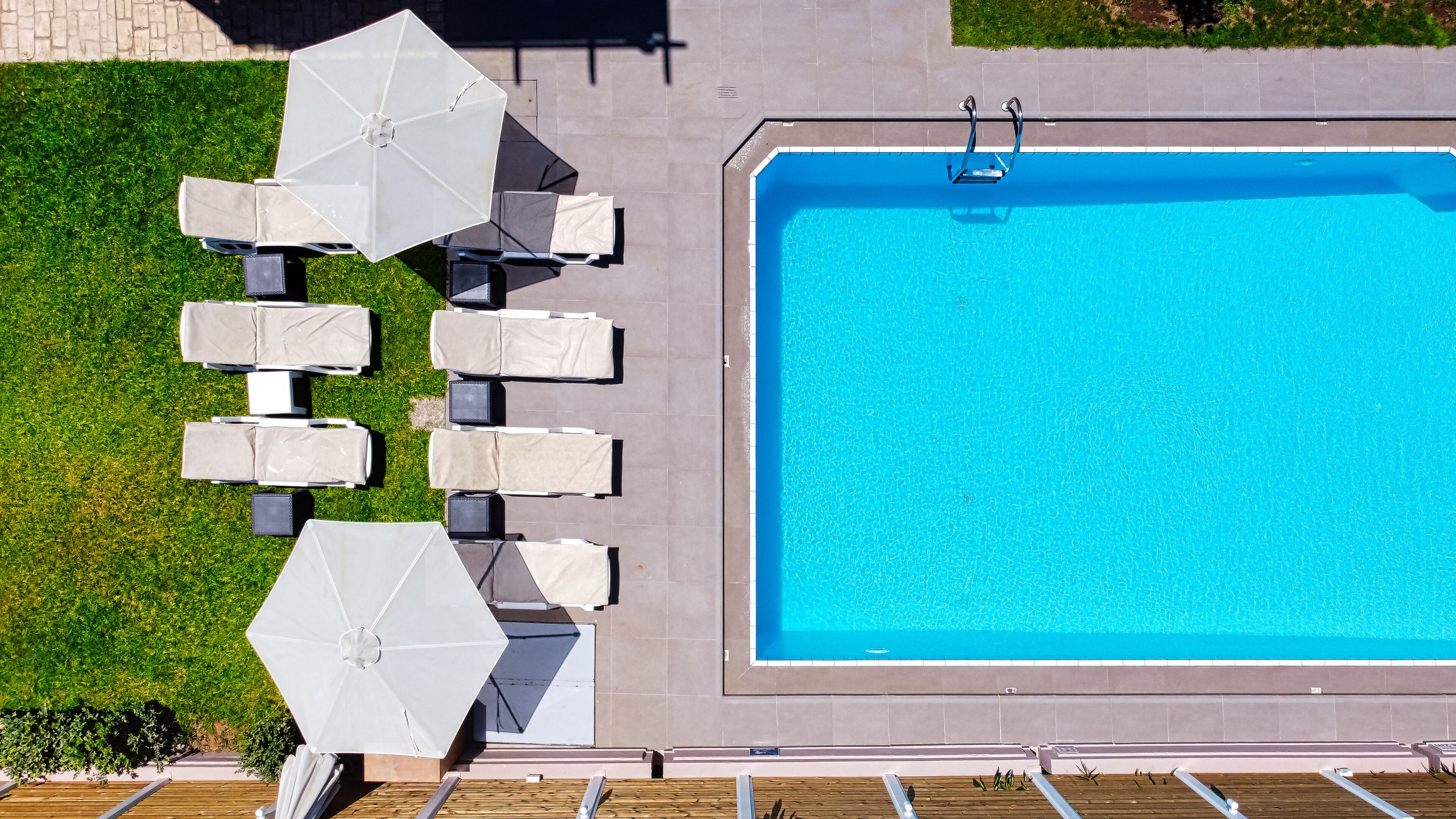 Eine Vogelperspektive auf einen Swimmingpool mit Liegestühlen und Sonnenschirmen rundherum.