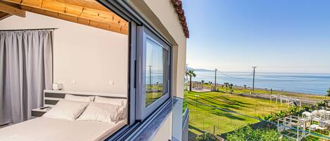 A bedroom with a large window overlooking a grassy area and the sea.