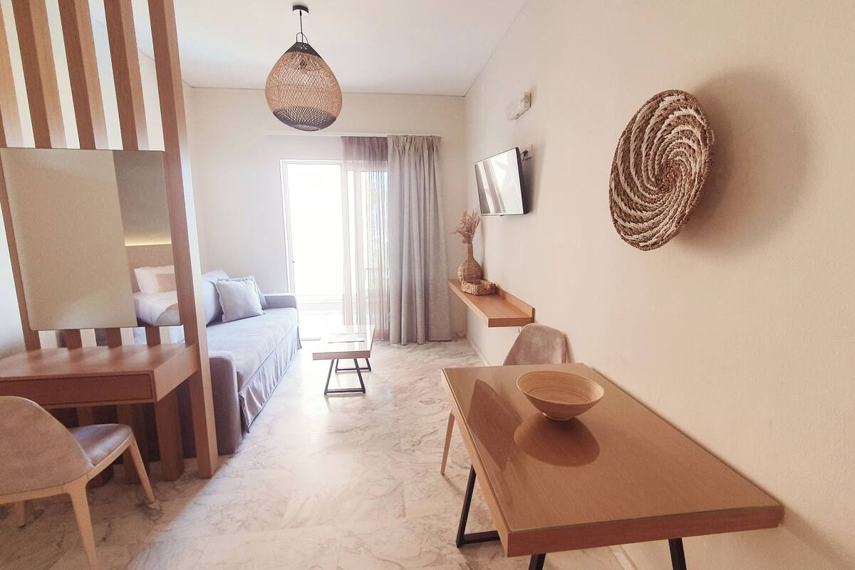 A modern hotel room with a bed, a desk, a chair, a TV, and a decorative wall hanging.