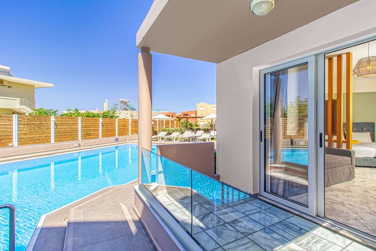 A modern hotel room with a glass door leading to a pool area, a balcony with a view of the pool, and a well-maintained garden.