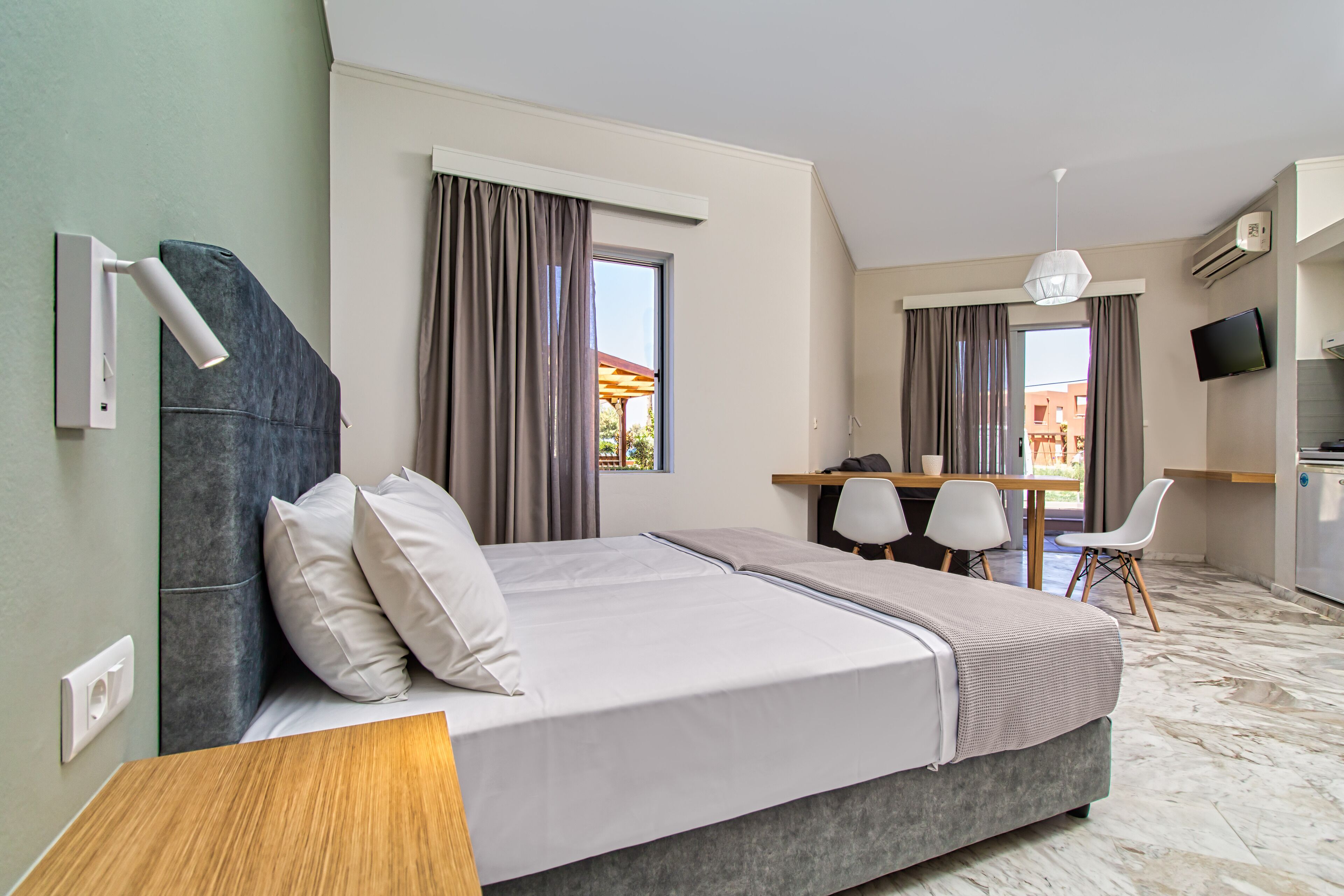 A modern hotel room with a bed, desk, chairs, and a TV.