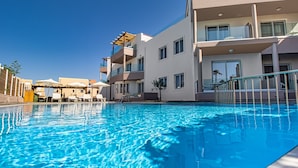 A swimming pool with clear blue water, surrounded by modern buildings with balconies and large windows. - Oliva Beach Studios & Apartments (Platanias)