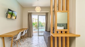 A modern room with a wooden desk, white chairs, a large mirror, and a view of a pool and greenery outside. - Oliva Beach Studios & Apartments (Platanias)