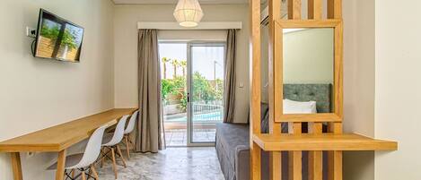 A modern room with a wooden desk, white chairs, a large mirror, and a view of a pool and greenery outside.