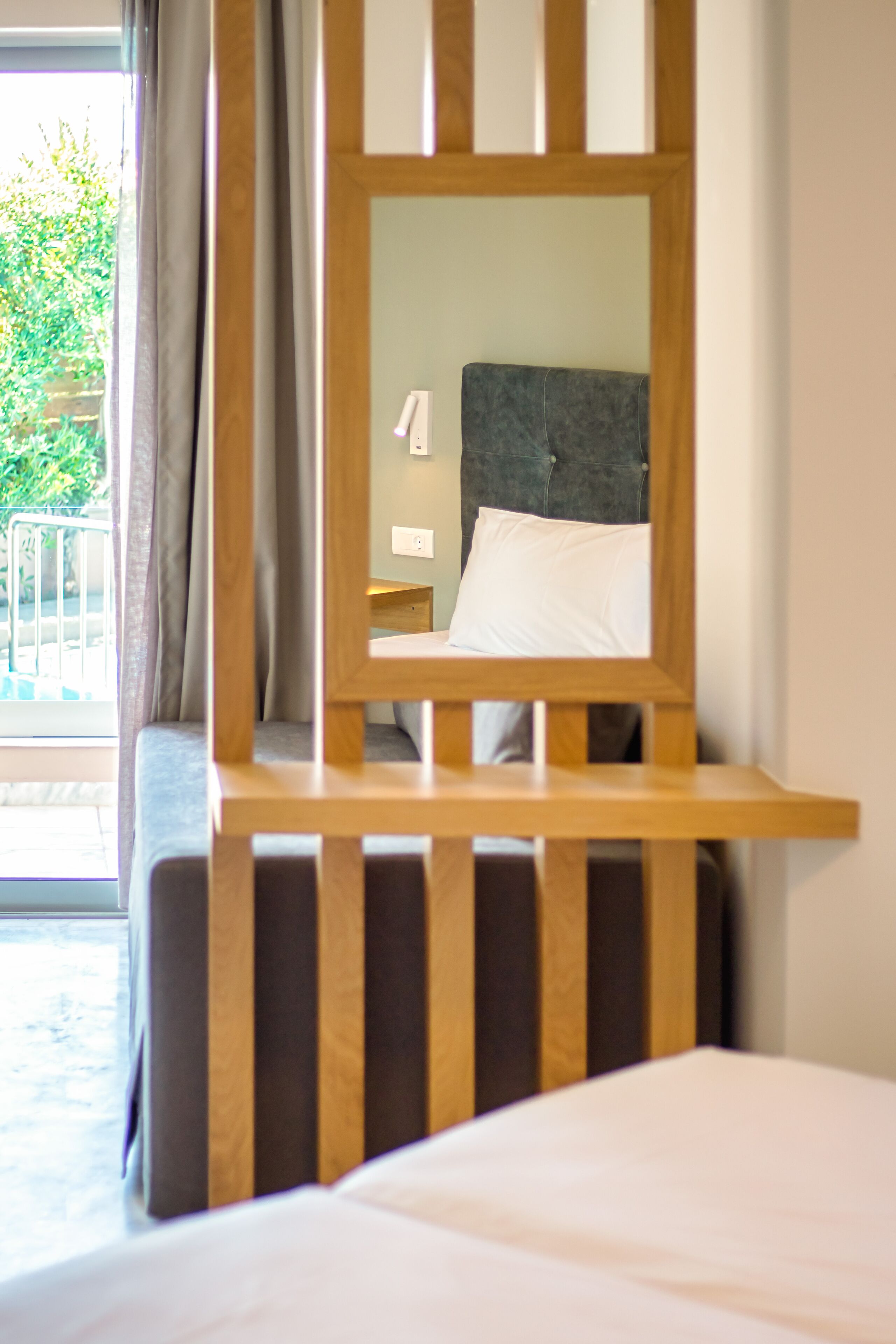 Habitación de hotel con cabecera de madera, cama con ropa blanca y vistas a un balcón con vegetación.