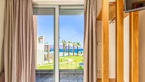 A room with a sliding glass door leading to a balcony with a view of palm trees and a building. - Oliva Beach Studios & Apartments (Platanias)