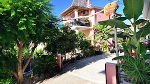 Ein Wohngebäude mit Balkon, umgeben von üppigem Grün und blauem Himmel.