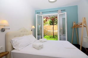 Quarto com cama, duas luminárias de cabeceira, um cavalete de madeira e vista para um jardim através de uma porta aberta.