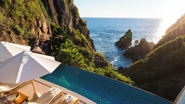 Piscina con vista al océano, sillas de descanso y sombrillas.