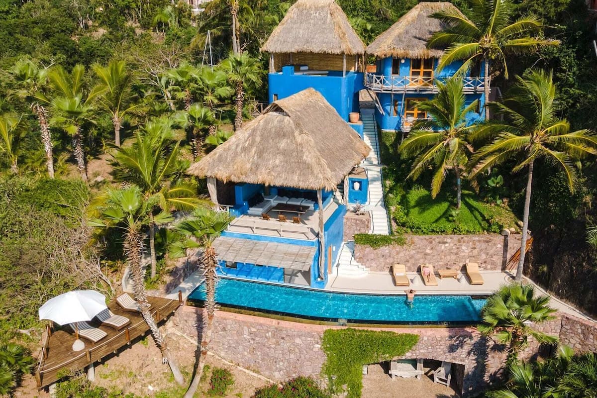 Ein Resort mit Pool, strohgedeckten Gebäuden und Palmen.