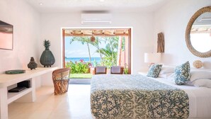 Un dormitorio con cama, un banco, una silla, un ventanal grande y vista al océano.