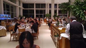 A spacious restaurant with multiple tables and chairs, large windows, and a bar area. - Charming 2 bedroom Apartment within Bahia Principe Resort (Akumal)