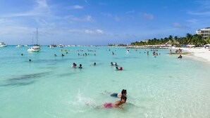 A beach with clear turquoise water, people swimming and sunbathing, and boats in the distance. - Charming 2 bedroom Apartment within Bahia Principe Resort (Akumal)