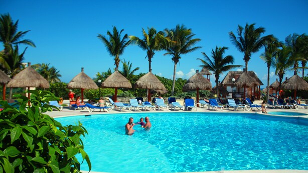 A swimming pool with lounge chairs and thatched umbrellas. - Charming 2 bedroom Apartment within Bahia Principe Resort (Akumal)