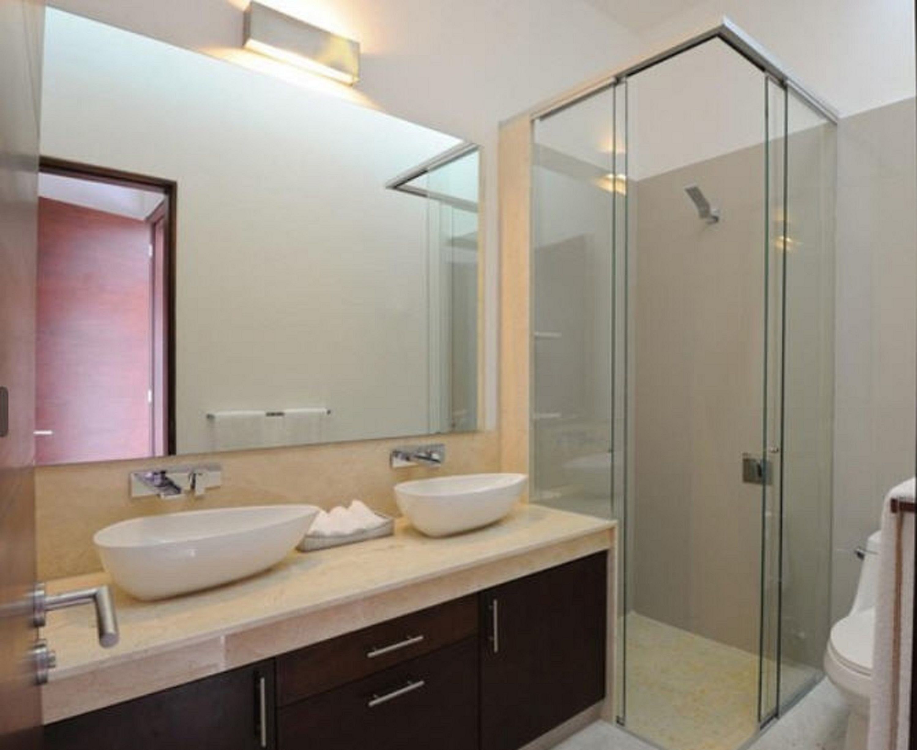 Une salle de bain moderne avec deux grands lavabos, une douche en verre et un grand miroir au-dessus du meuble-lavabo.