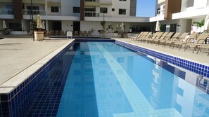 A swimming pool with blue tiles, surrounded by lounge chairs and potted plants.
