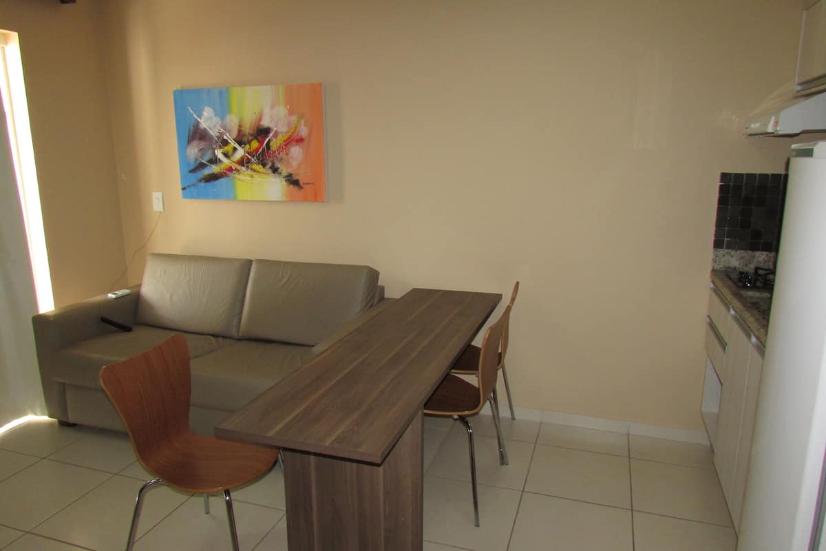 A dining area with a wooden table and chairs, a grey sofa, and a colorful abstract painting on the wall.