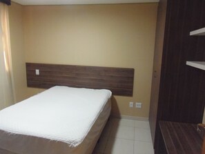 A bedroom with a bed, a wooden headboard, a small bedside table, and a wall-mounted shelf.