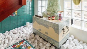 Quarto com escada de madeira, uma estátua de Buda sobre um pedestal e chão de azulejos com pedrinhas brancas.