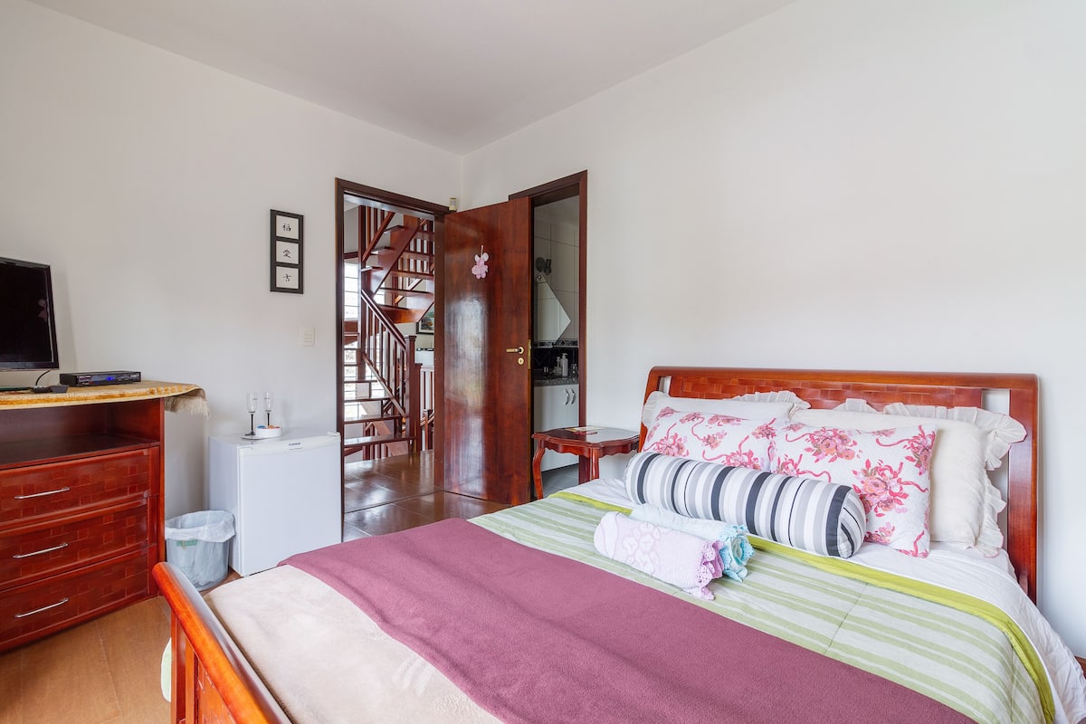A bedroom with a bed, wooden dresser, desk, and a small refrigerator.