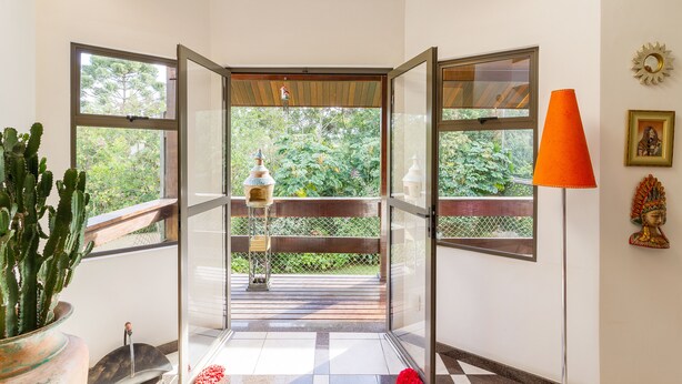 Quarto com vista para o verde através de grandes janelas, uma planta de cacto, um abajur e uma estátua na parede.