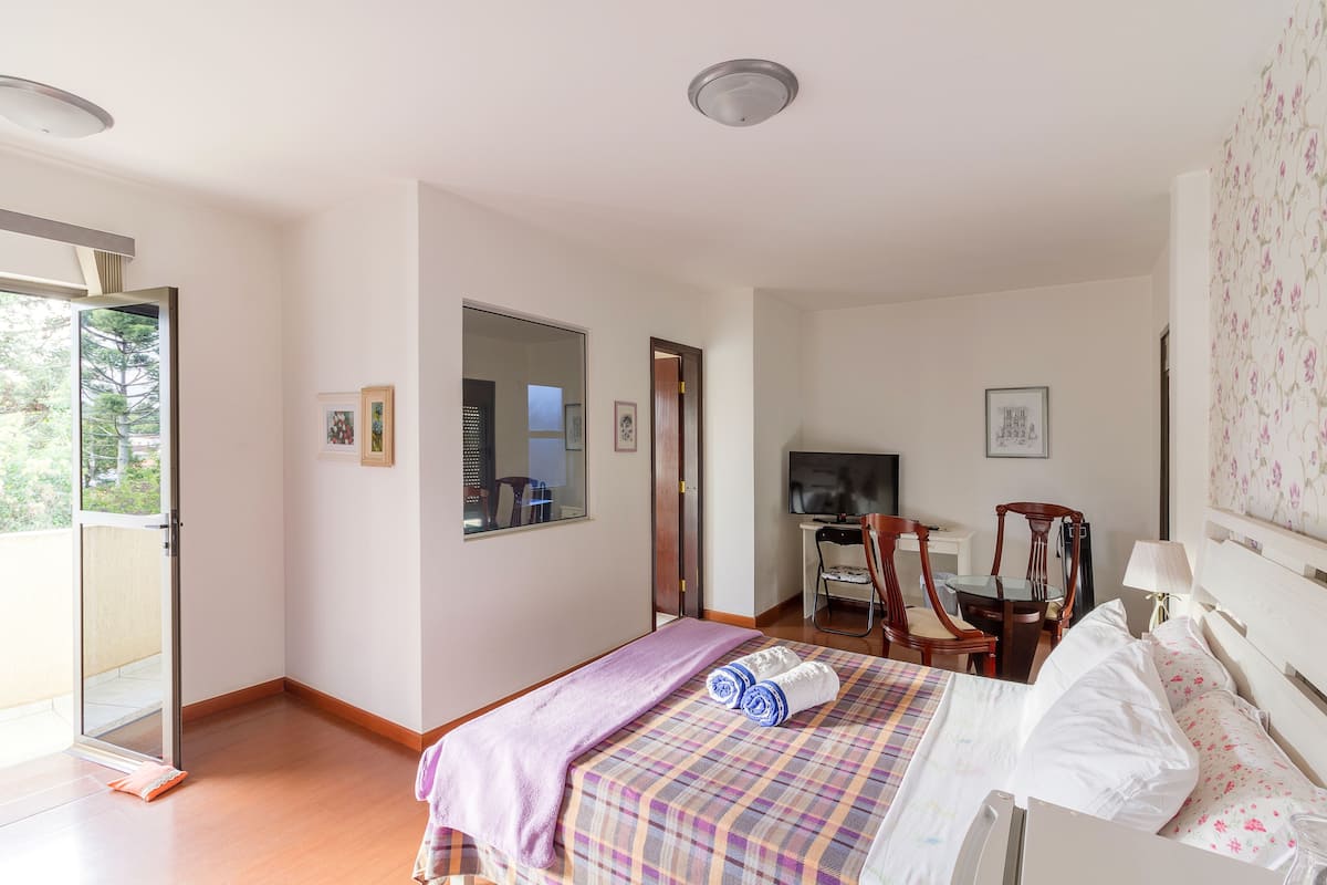 A bedroom with a bed, a desk, a chair, a television, and a door leading to a balcony.