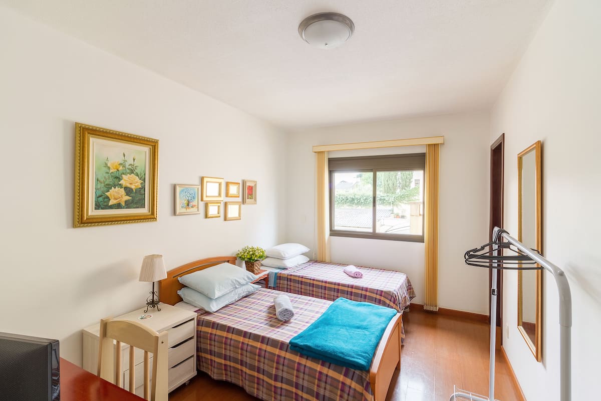 A room with two beds, a desk, a chair, a TV, and a window with curtains.