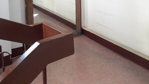 Ein Zimmer mit einem spiegelnden Holzrahmen, einem Holzstuhl und einer weißen Wand.