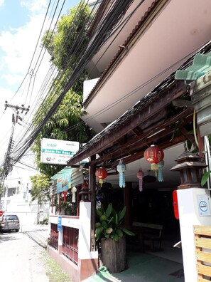 A building with a sign for a room for rent, a wooden structure with hanging lanterns, and a parked car. - Inter Inn Chiangmai (Chiang Mai)