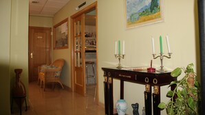 Una habitación con una silla de madera, una mesa con velas, un cuadro y una puerta que da a otra habitación.