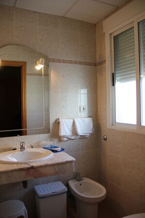 A bathroom with a sink, mirror, bidet, and a window with blinds. - Hotel Dora (Plasencia)