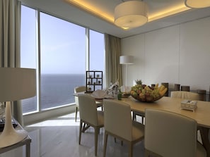 A modern hotel room with a large panoramic window, a dining table with chairs, a fruit bowl, and a lamp. - Novotel Jazan (Jizan)