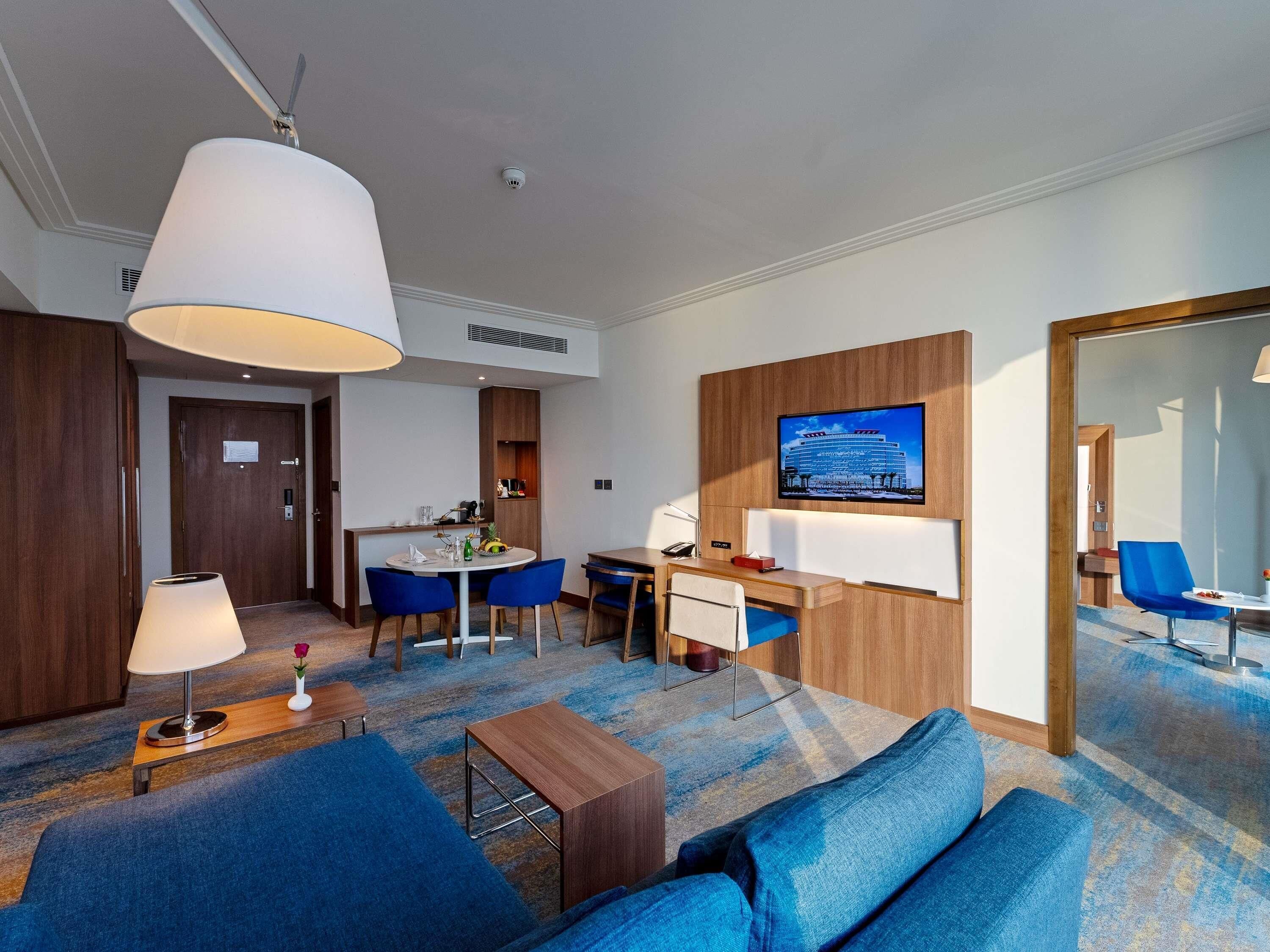 Habitación de hotel con sofá, escritorio, televisor, zona de comedor y baño.