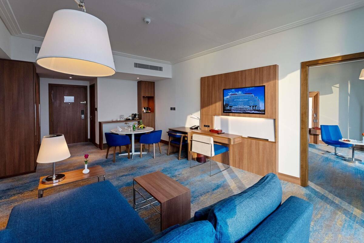 Habitación de hotel con sofá, escritorio, televisor, zona de comedor y baño.