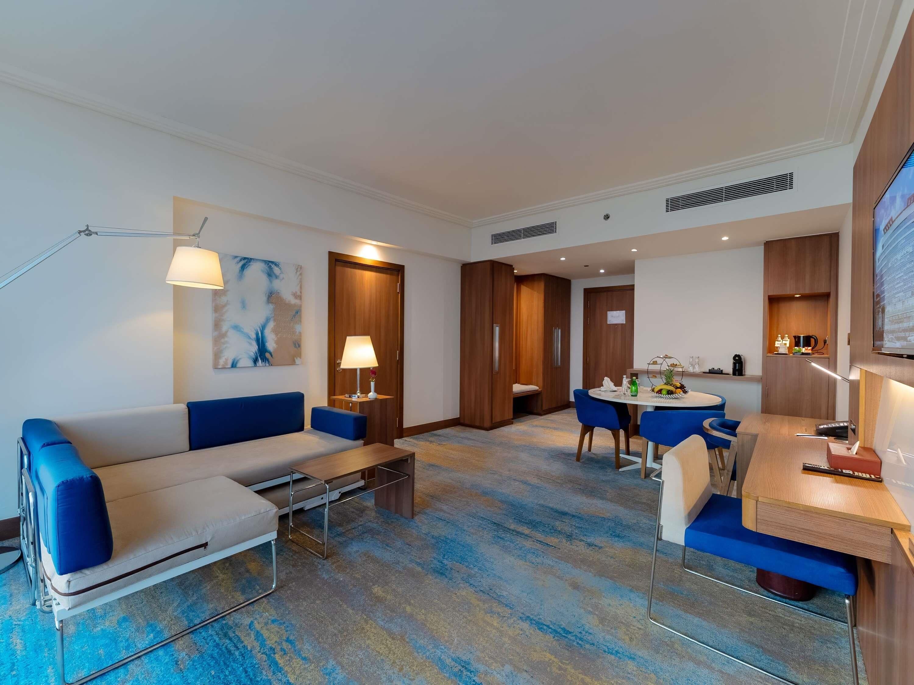 A modern hotel room with a sofa, a dining table, and a TV.