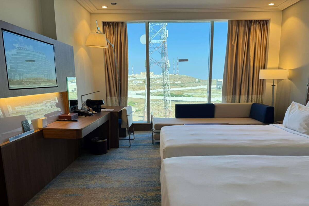 Una habitación de hotel con cama, escritorio, silla y televisión en la pared.