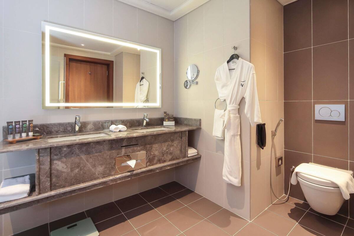 Un baño moderno con un espejo grande, una bata colgada en la pared, un inodoro y un lavamanos con artículos de aseo.
