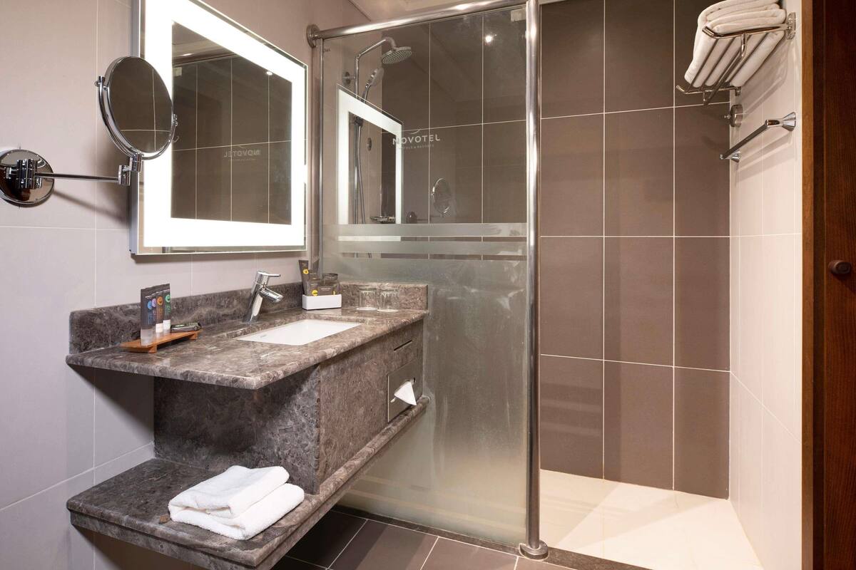 Un baño moderno con ducha de vidrio, lavamanos de mármol, espejo y toallero.