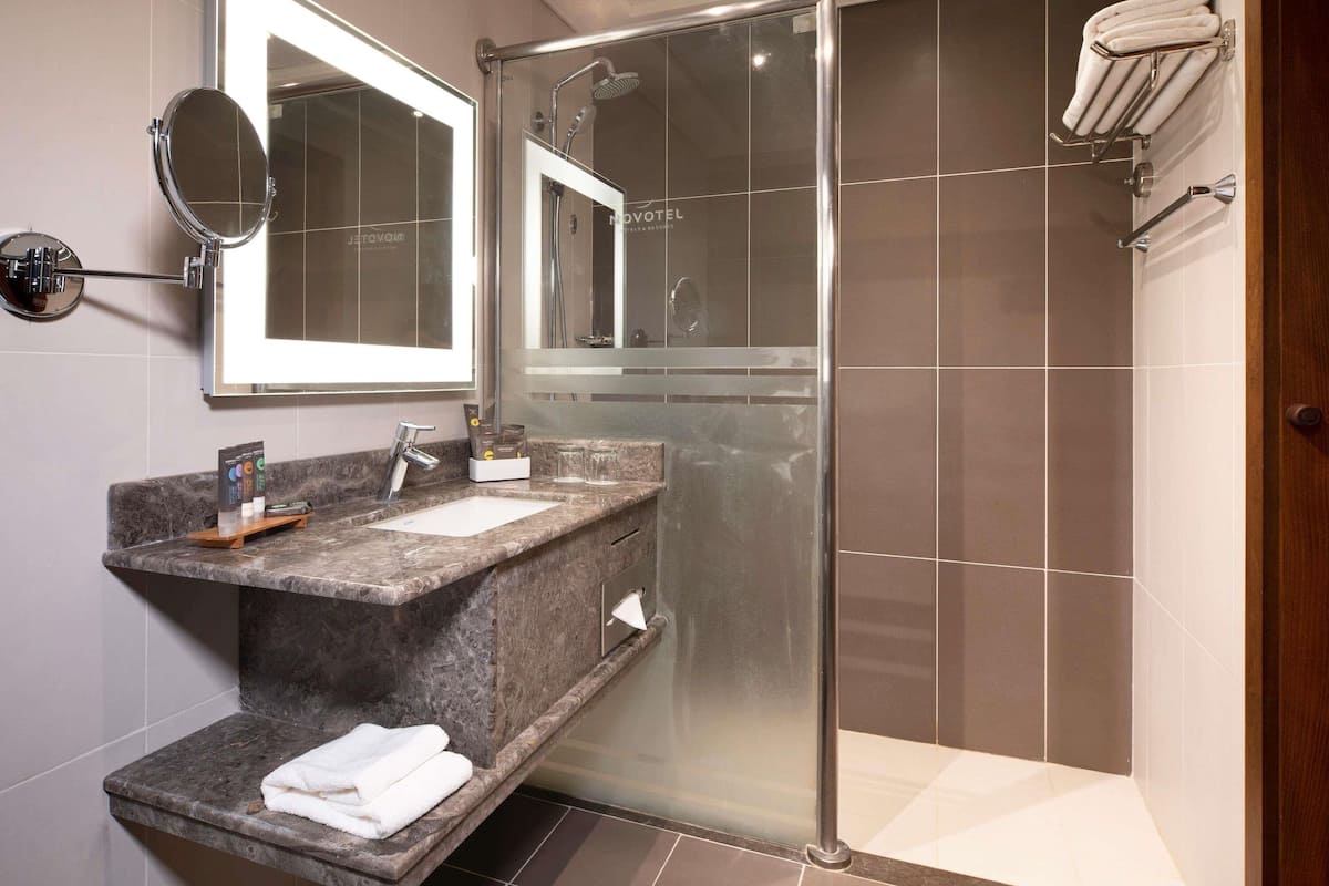 A modern bathroom with a glass-enclosed shower, a marble sink, a mirror, and a towel rack.