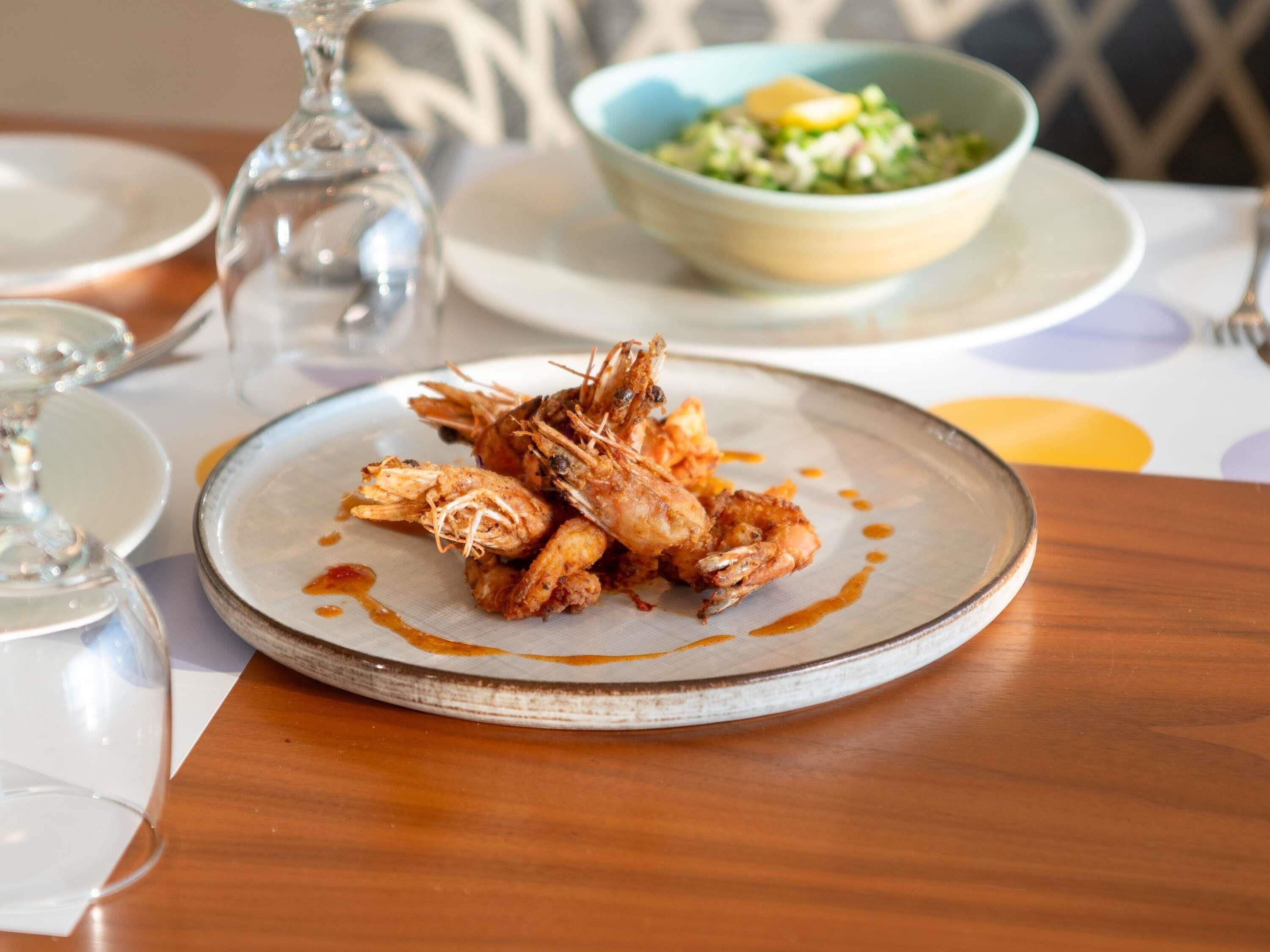 Un plato de camarones fritos sobre un plato de cerámica con salsa, acompañado de una ensalada en un tazón y un vaso de agua sobre una mesa.